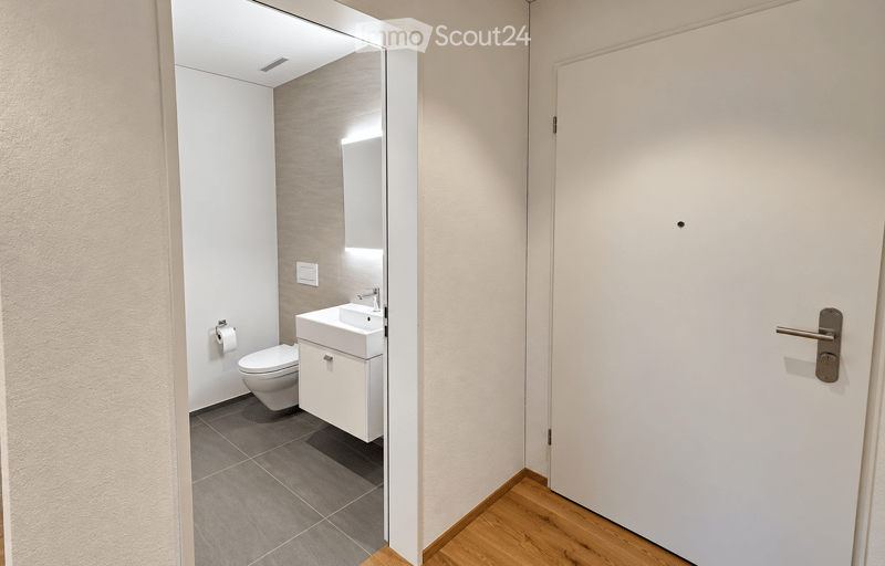 Modern bathroom with a white sink, toilet, and mirror, featuring a grey tiled floor and light-colored walls.