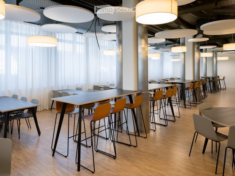 Modern, spacious room with wooden flooring, large round pendant lights, and multiple tables with chairs and stools arranged throughout.