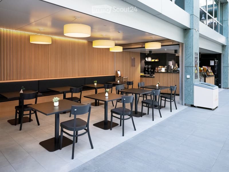 Modern outdoor seating area with tables, chairs, and small potted plants, featuring a bar area in the background with various appliances and decor.