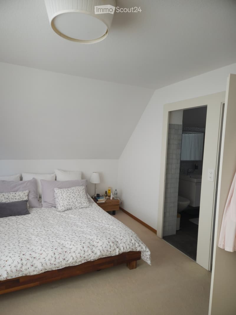 Cozy bedroom with a wooden bed, multiple pillows, a nightstand with a lamp, and an open door leading to a bathroom.