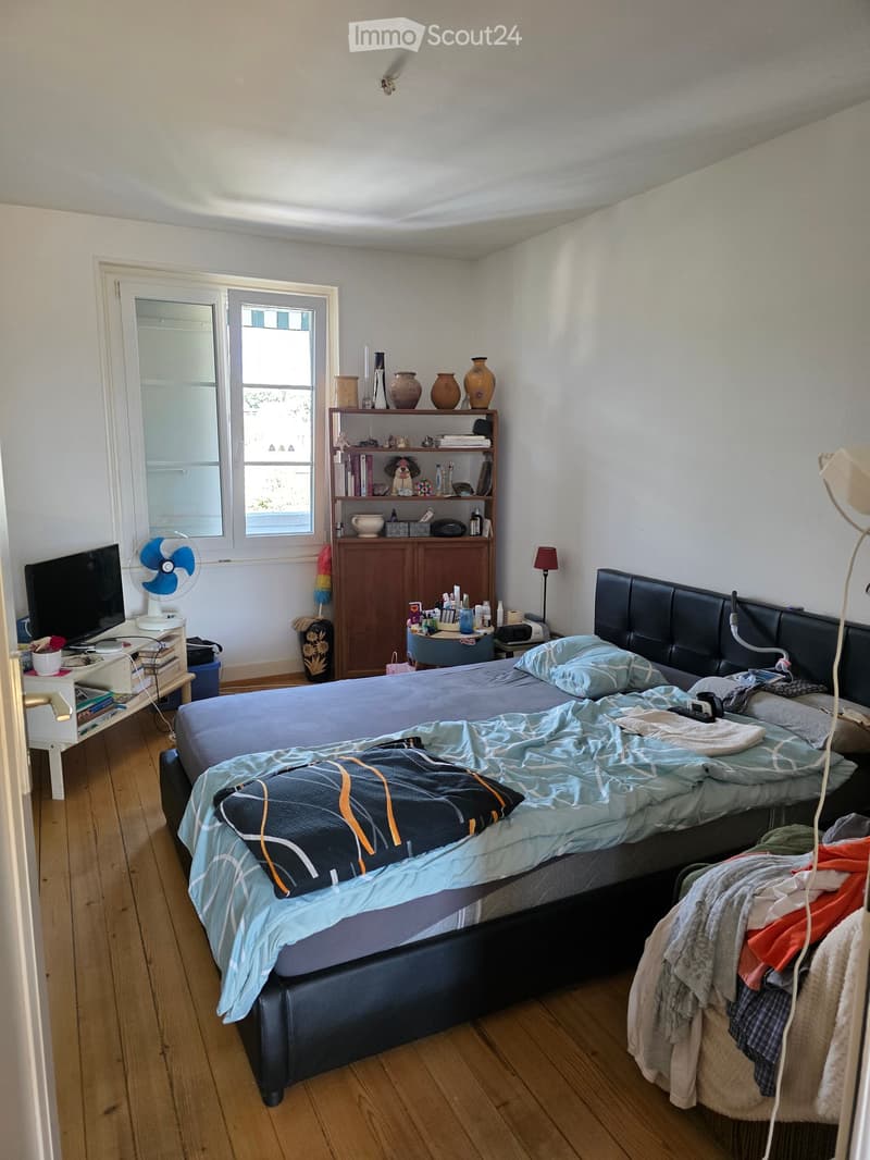 A furnished bedroom with a large bed, nightstand, fan, table, chair, cabinet, shelf, vases, and a lamp.