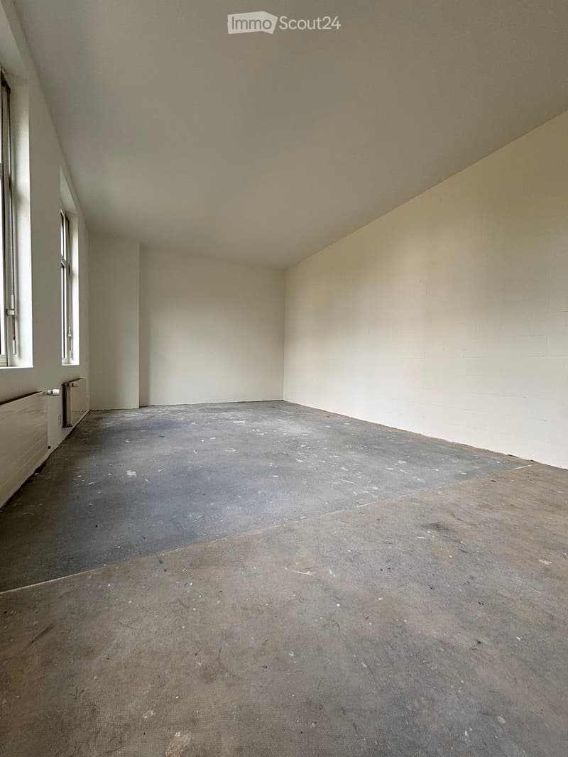 Empty room with bare walls and concrete floor, featuring a small window and a radiator on the left side.