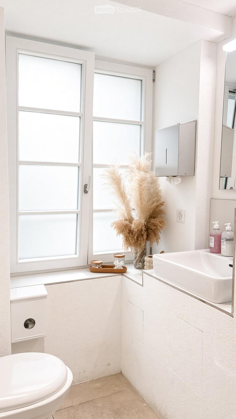 Modern bathroom with white walls, a toilet, a sink, a mirror, and a decorative vase on the windowsill.