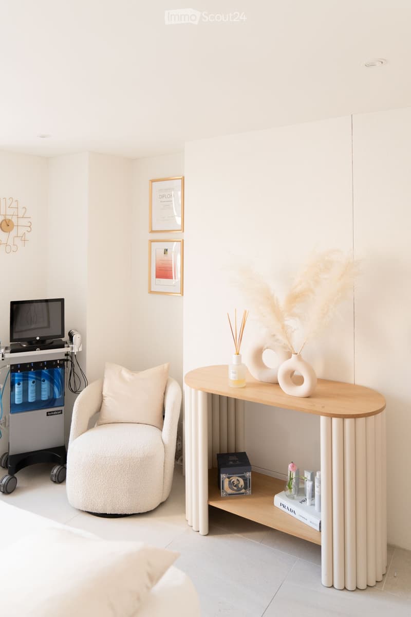 A modern, minimalistic room with a round wooden table, a plush chair, decorative vases, a screen, and framed certificates on the wall.