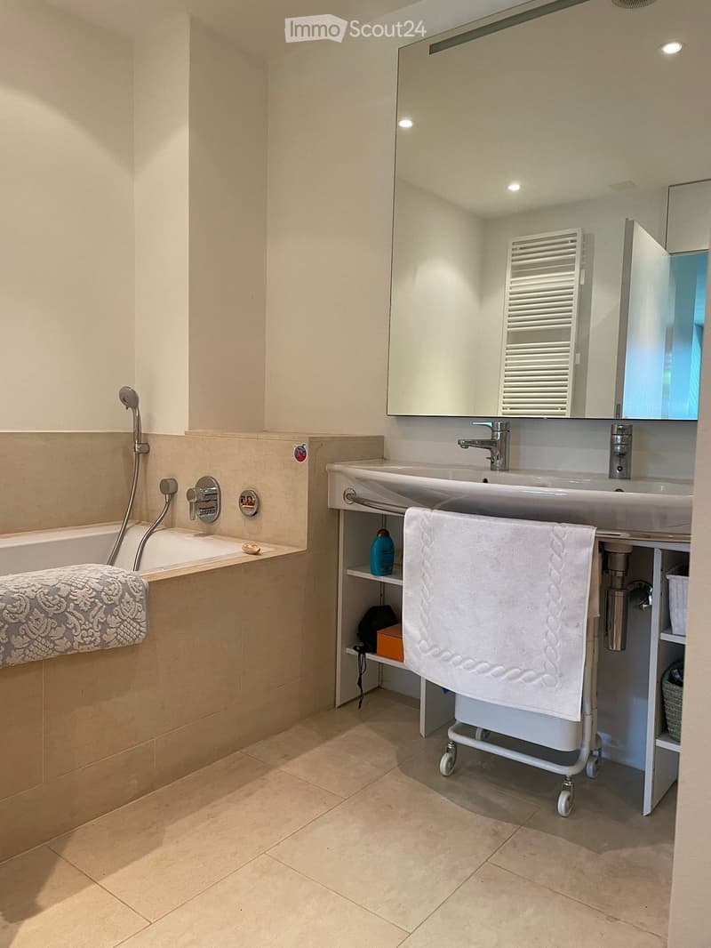 modern bathroom with bathtub, large mirror, sink with trolley, built-in shelf, and towel racks