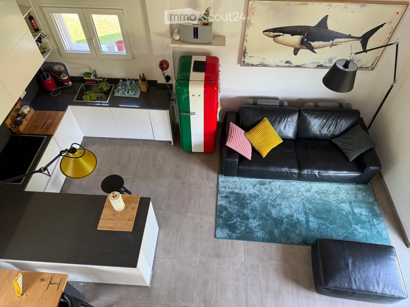 Open-plan living and kitchen area with a black leather sofa, colorful cushions, a small wooden table, a colorful refrigerator, and a modern kitchen setup with a sink and countertop.