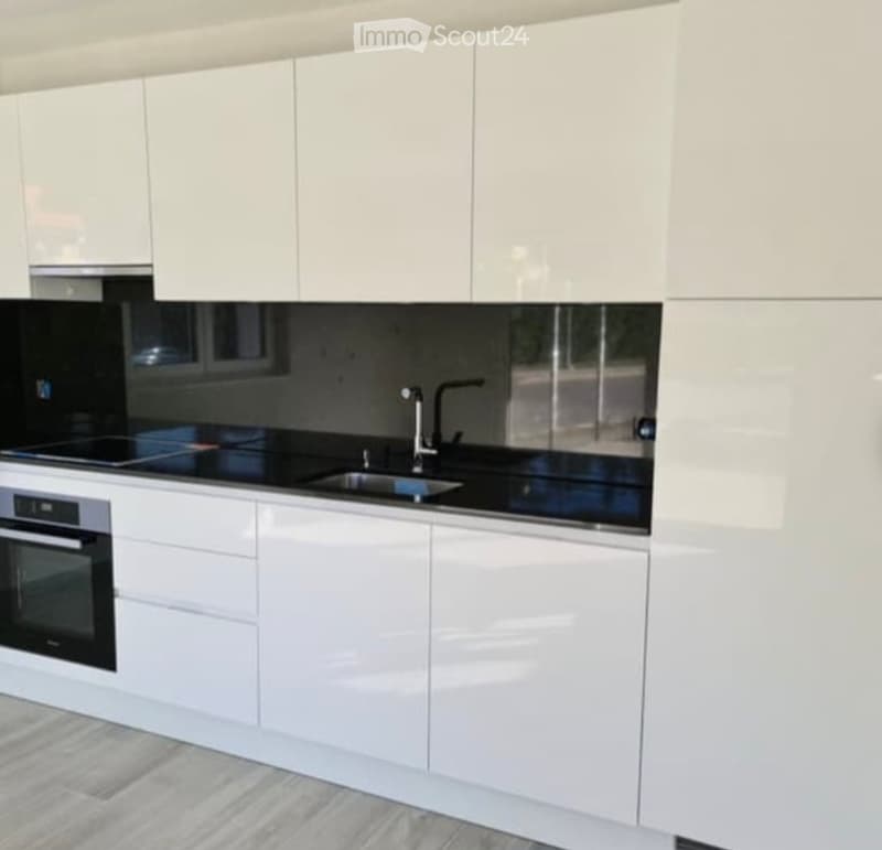 Modern kitchen with white cabinets, black countertops, and stainless steel appliances including an oven and a sink with a faucet.