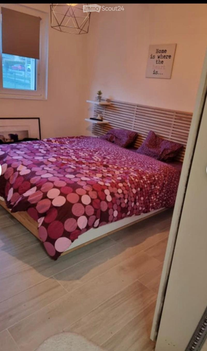 Cozy bedroom with a wooden bed, patterned bedding, nightstand, shelves, and a decorative lamp.