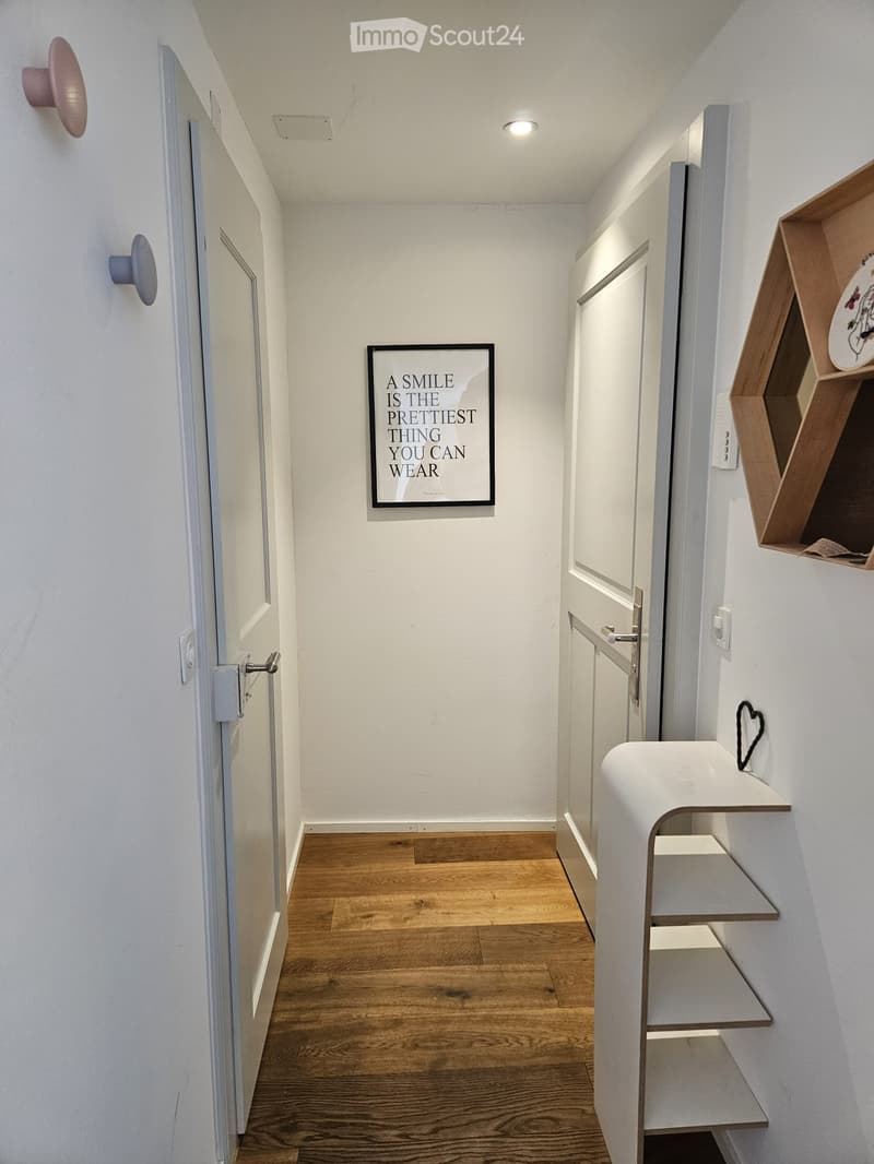 Modern hallway with wooden flooring, white walls, and built-in shelving units. Features a framed motivational quote and decorative wall-mounted items.