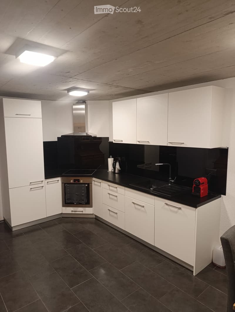 Modern kitchen with white cabinets, black countertops, stainless steel appliances, and dark tiled flooring.