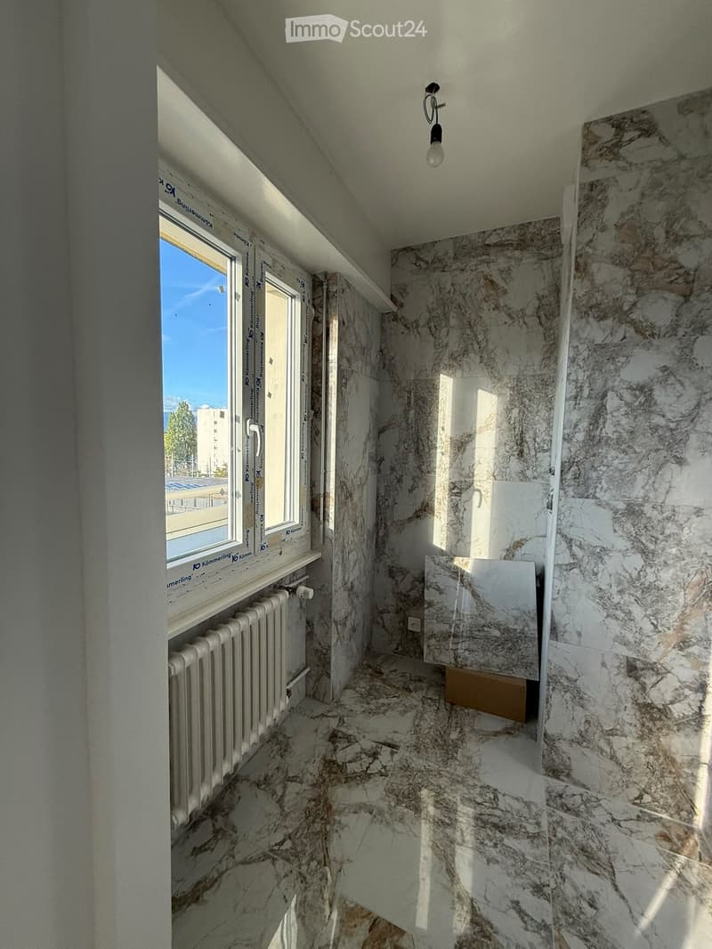 Narrow hallway with marble walls and floor, a radiator on the left, and a window at the end letting in natural light.