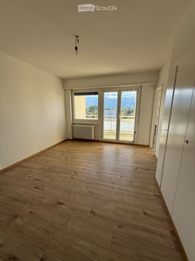 Empty room with wooden flooring, white walls, a window with a view, and a radiator. No furniture or equipment present.