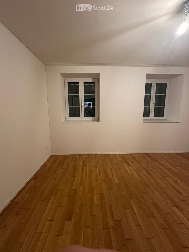 Empty room with wooden flooring, white walls, and two windows with white frames.