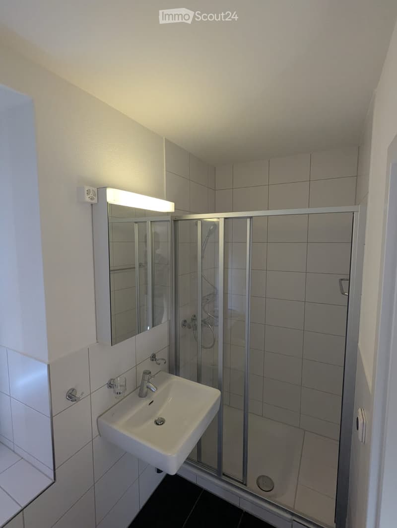 Modern bathroom with a white sink, mirror with built-in lighting, and a glass-enclosed shower area.