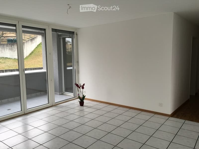 Empty room with tiled floor, white walls, large sliding glass doors leading to a balcony, and a small potted plant near the entrance.
