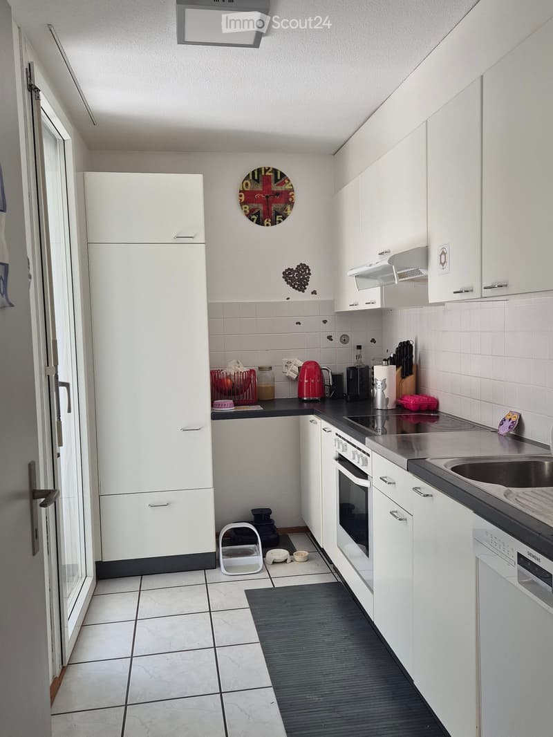 Modern kitchen with white cabinets, stainless steel appliances, and a black countertop. Features include a refrigerator, oven, dishwasher, sink, and various kitchen items such as a coffee maker, toaster, and cat supplies.