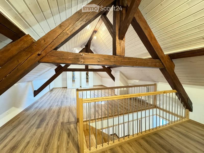 Staircase with wooden beams and a metal railing, leading to a room with white walls and wooden flooring.