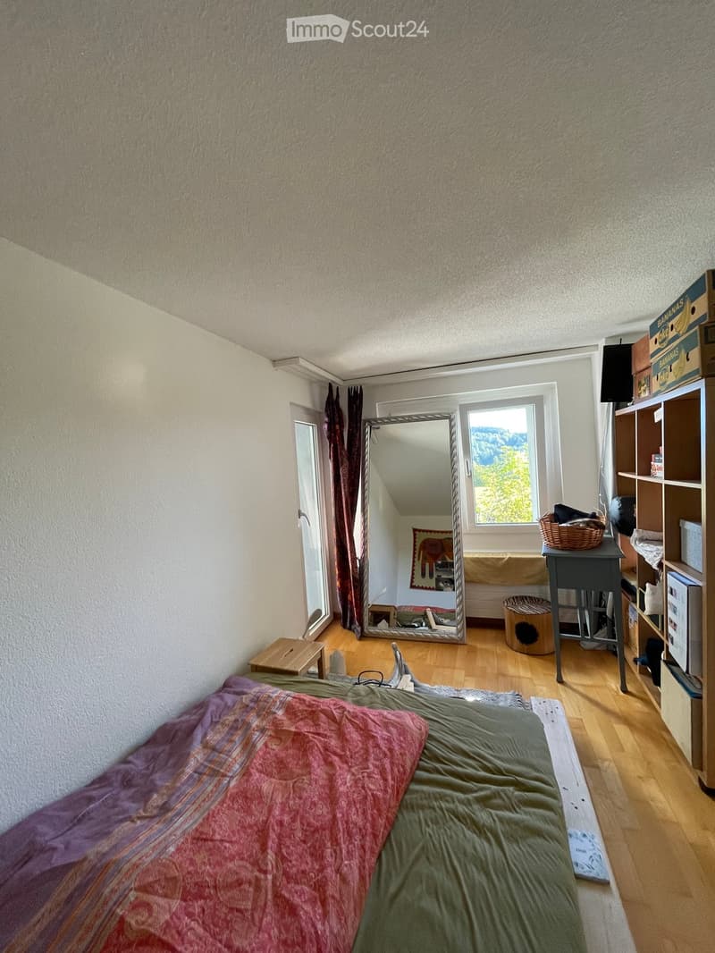 Cozy bedroom with wooden flooring, a bed with colorful bedding, a large mirror, a small table, shelves, and a cat tree.