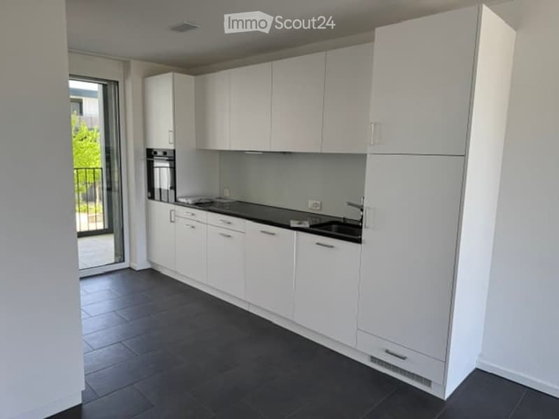Modern kitchen with white cabinets, black countertops, and a built-in oven. Features a large window with a view of the balcony.