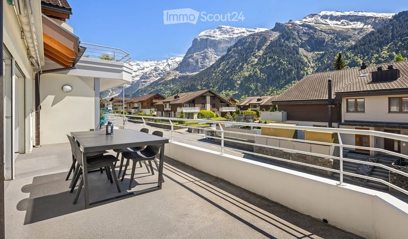 Balcony with a table and chairs, overlooking a scenic mountain view and town.