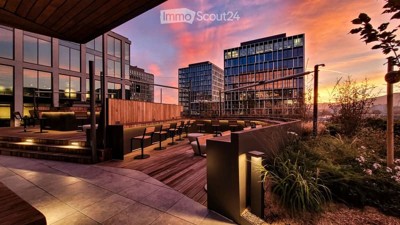 Modern rooftop terrace with wooden decking, seating area, and cityscape view at sunset.