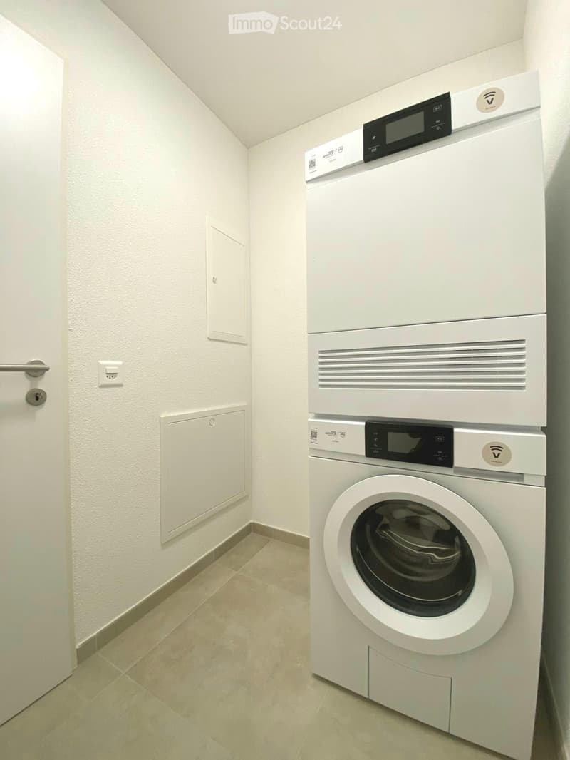 A small, clean room with a white washing machine and a white dishwasher stacked vertically, tiled floor, white walls, and a door.