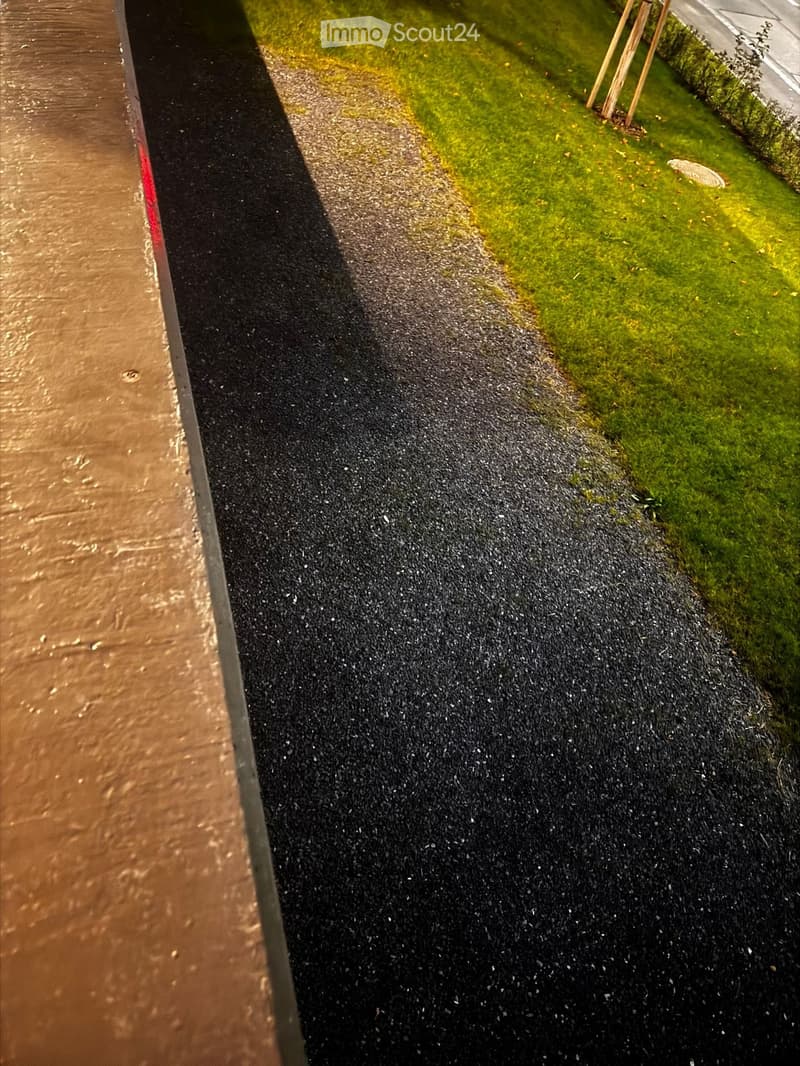 A paved pathway bordered by grass, with a water body on one side and a grassy area on the other.