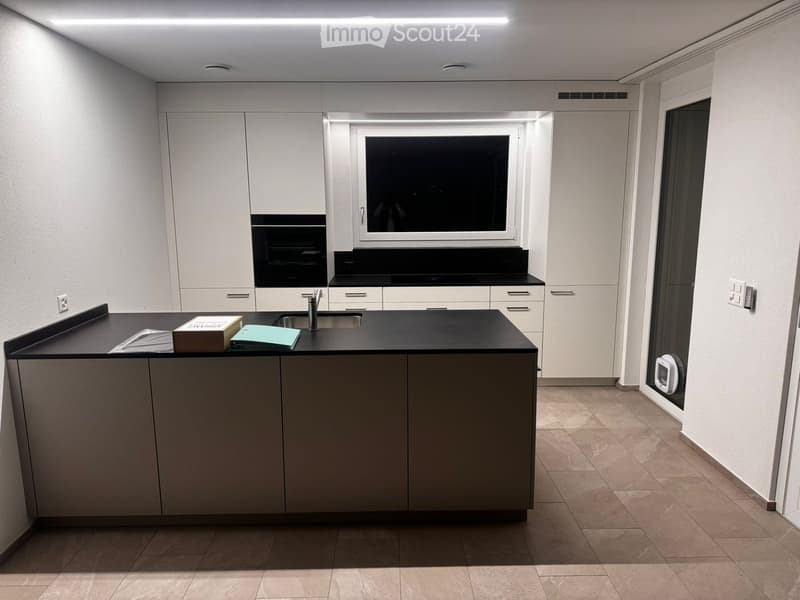 Modern kitchen with white cabinets, black countertops, and a central island. Features a sink, faucet, and a window above the counter.