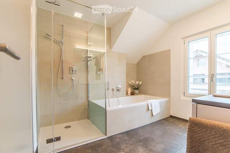 Modern bathroom with a large bathtub, glass-enclosed shower, and a small vase with white flowers on the counter.
