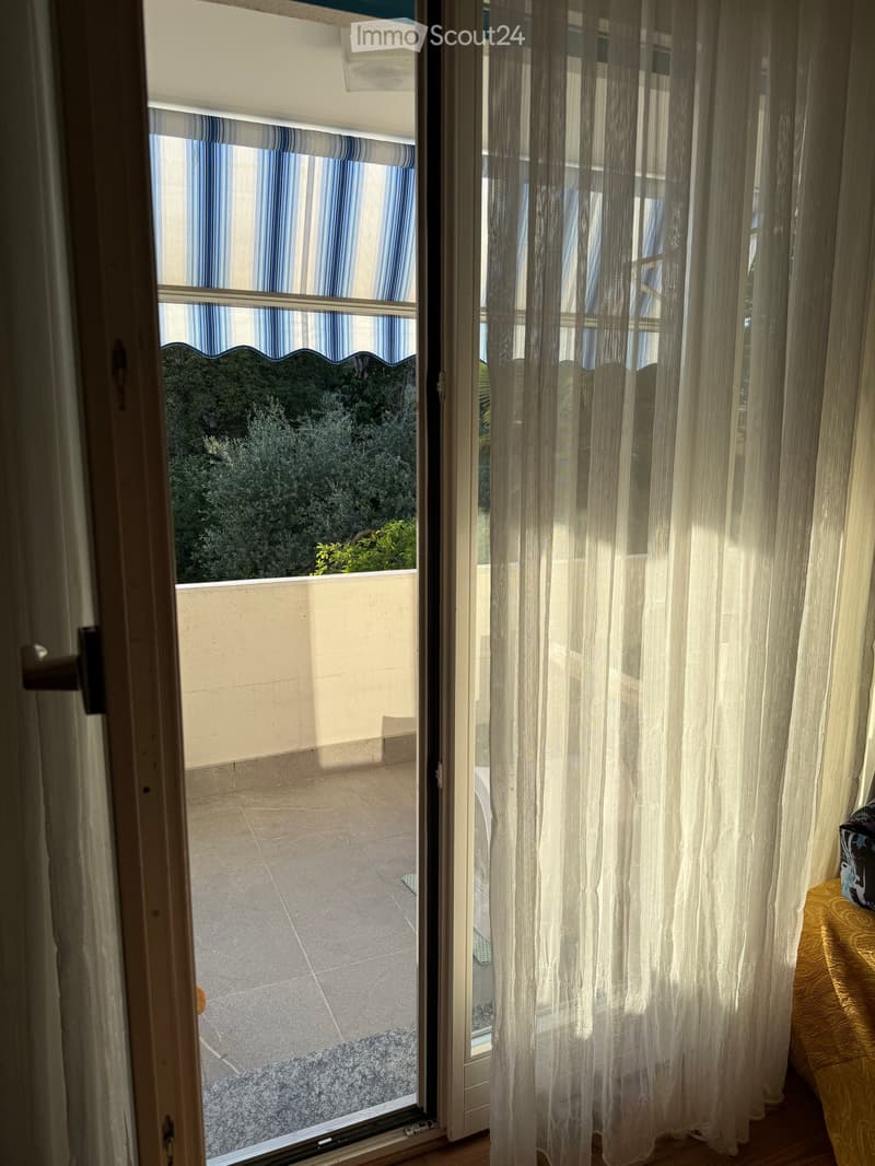 Balcony with tiled floor, striped curtains, and view of greenery outside.