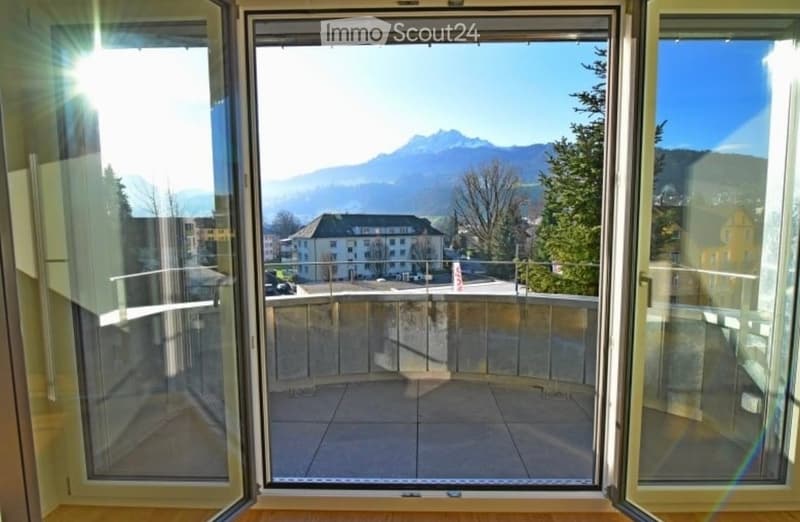 Balcony with glass railing, overlooking a scenic mountain view and town buildings.