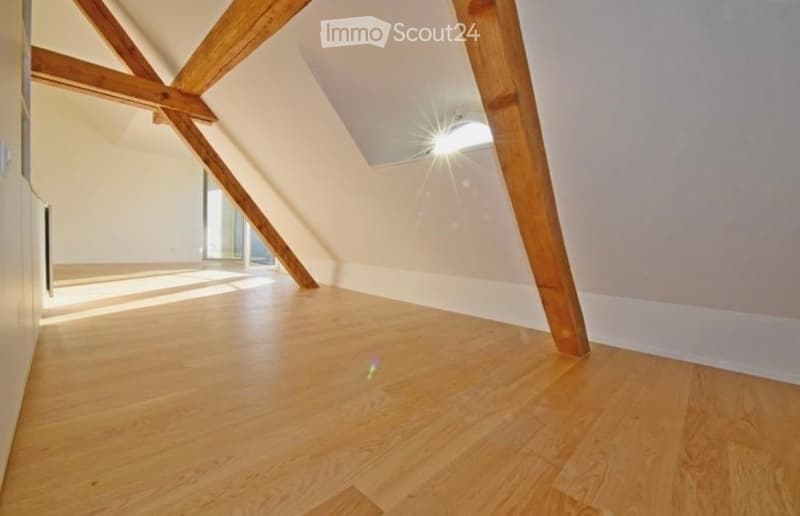 Empty attic room with wooden beams, wooden flooring, and large windows allowing natural light to enter.
