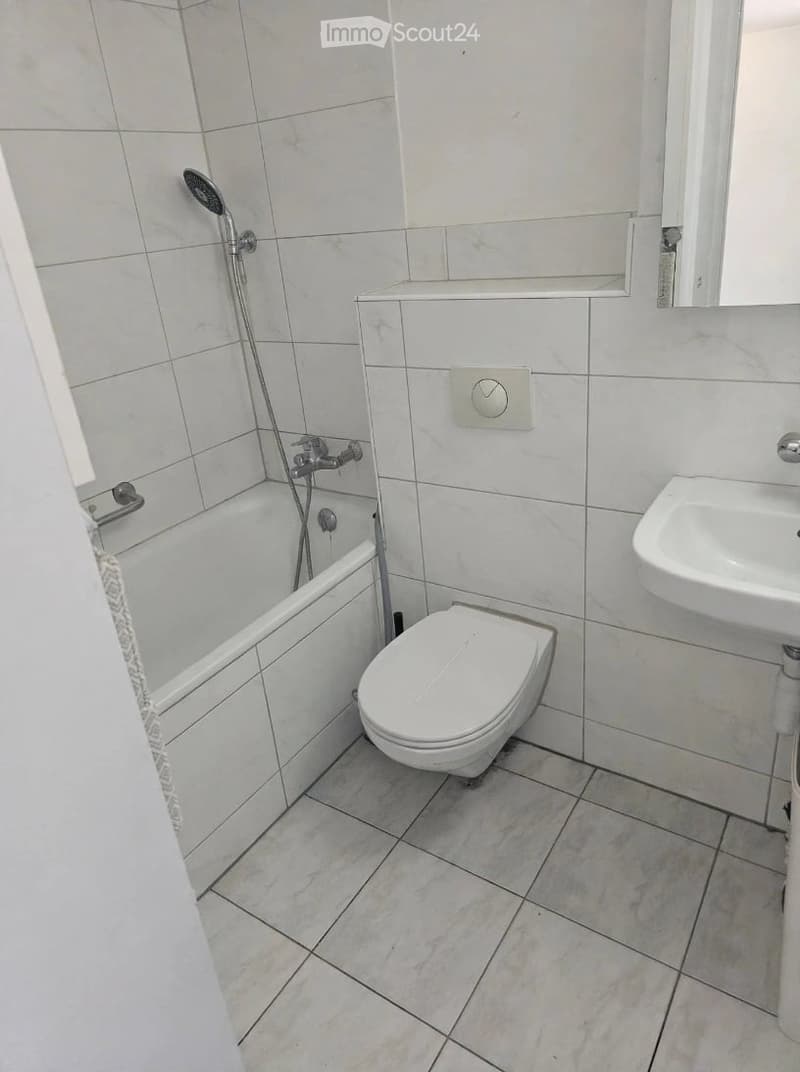 Modern bathroom with white tiles, a bathtub, toilet, sink, and a showerhead.
