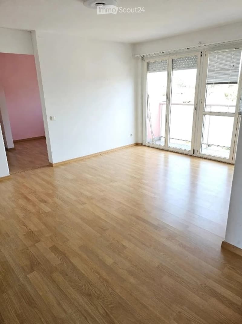 Empty room with wooden flooring, white walls, and large glass sliding doors leading to a balcony.