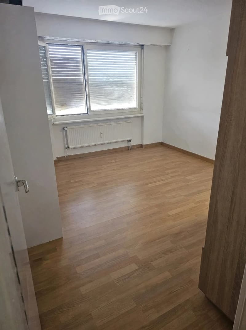 Empty room with wooden flooring, white walls, and a window with blinds. Radiator under the window.