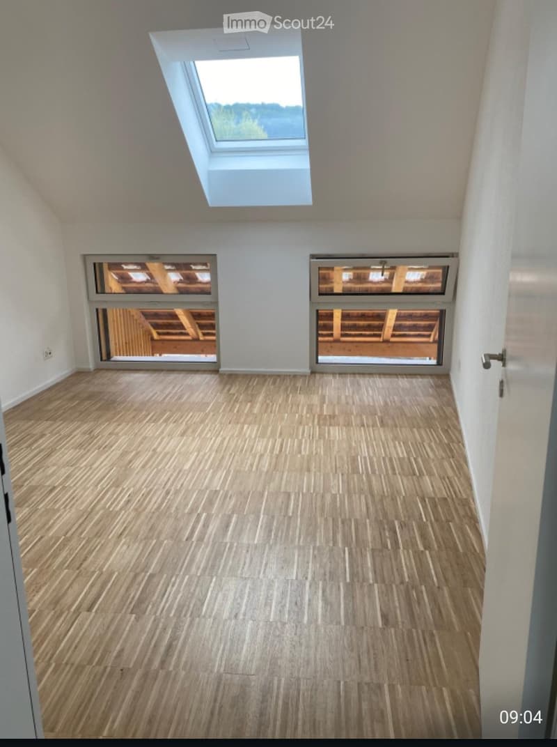 Empty room with wooden flooring, white walls, and large windows including a skylight, offering natural light.