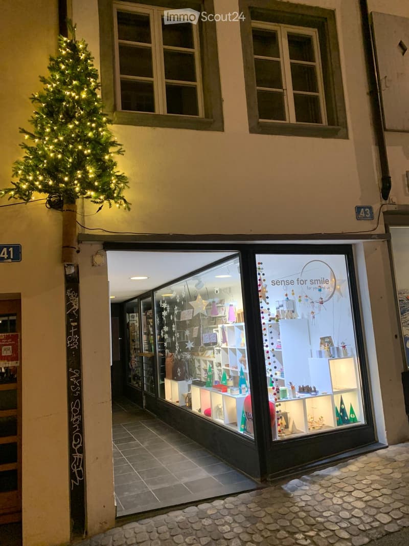Storefront with festive holiday decorations, including Christmas trees and ornaments displayed in the window, with a sign reading "sense for smile" visible.