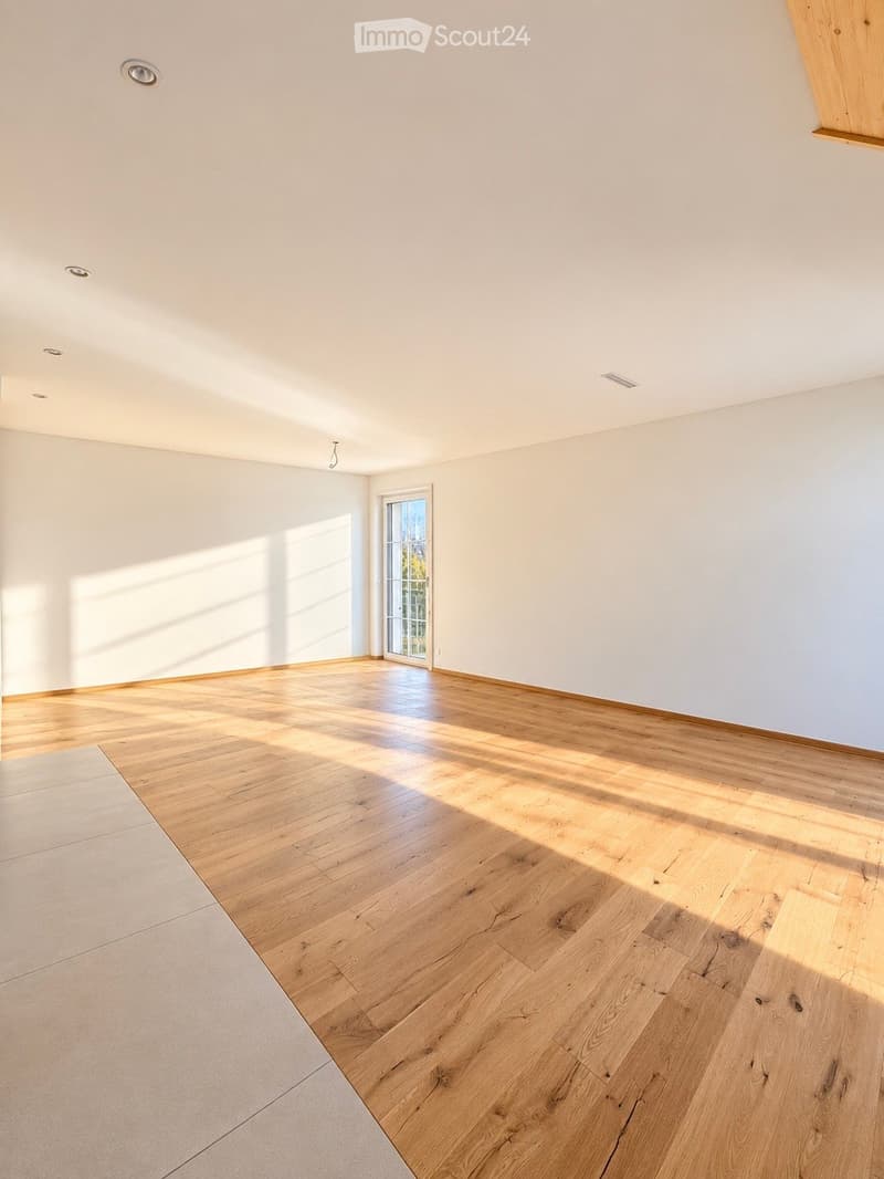 Empty room with light wooden flooring and white walls, featuring a large window allowing natural light to enter.