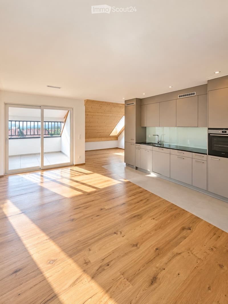 Open-plan space with light wooden flooring, modern kitchen cabinets, and a sliding glass door leading to a balcony.