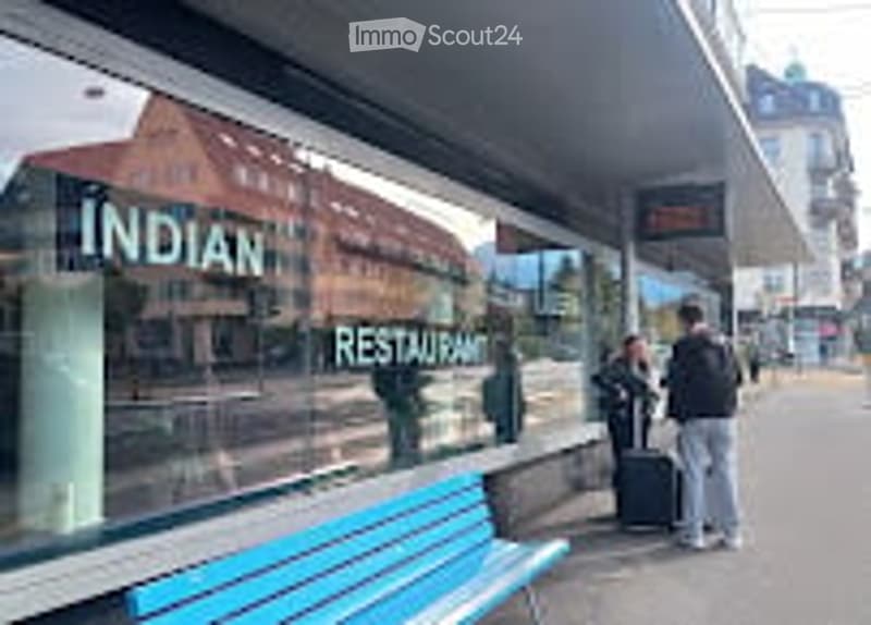 A public sidewalk with a blue bench, a restaurant sign reading "INDIAN RESTAURANT" visible in the background, and a few pedestrians.