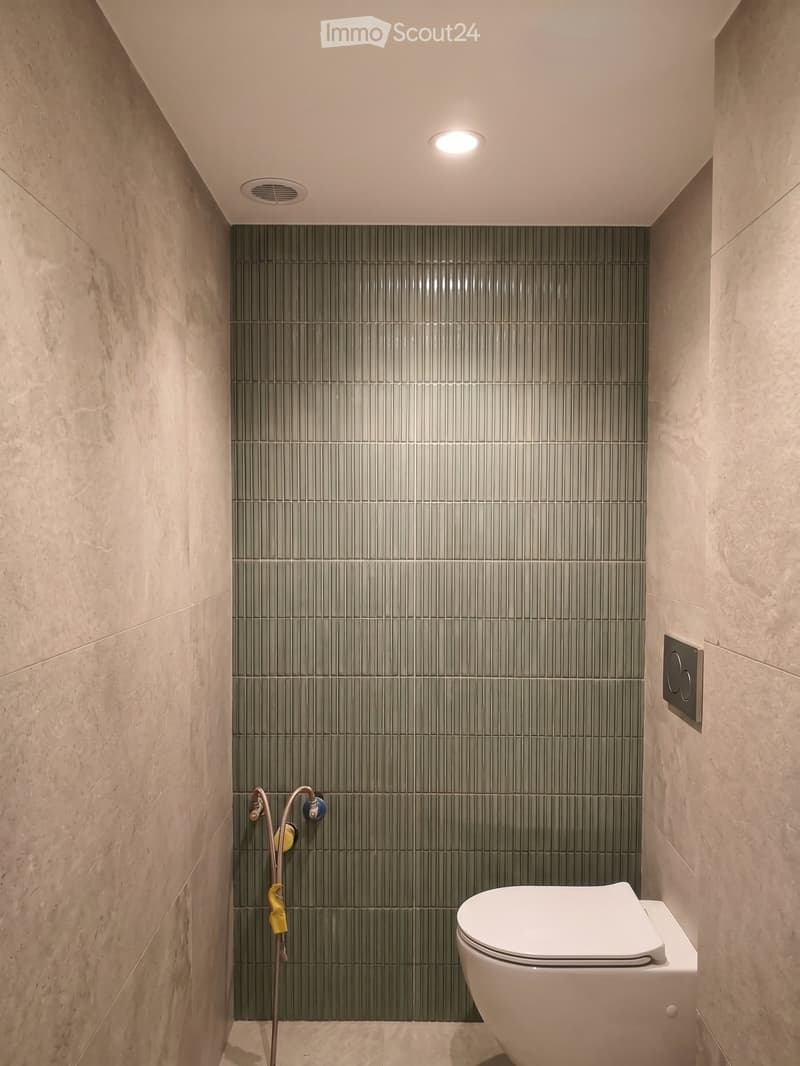 Modern bathroom with grey tiled walls, white toilet, and a sleek faucet.
