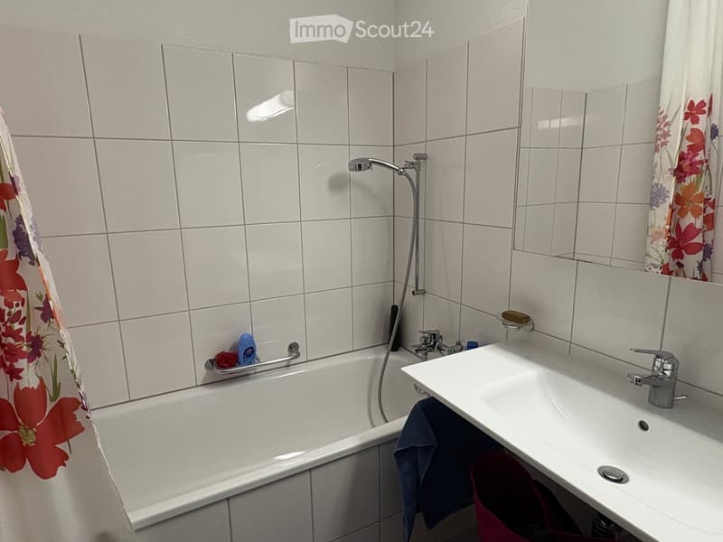 Bathroom with a bathtub, sink, mirror, and shower curtain. Includes a towel and soap dispenser on the sink.