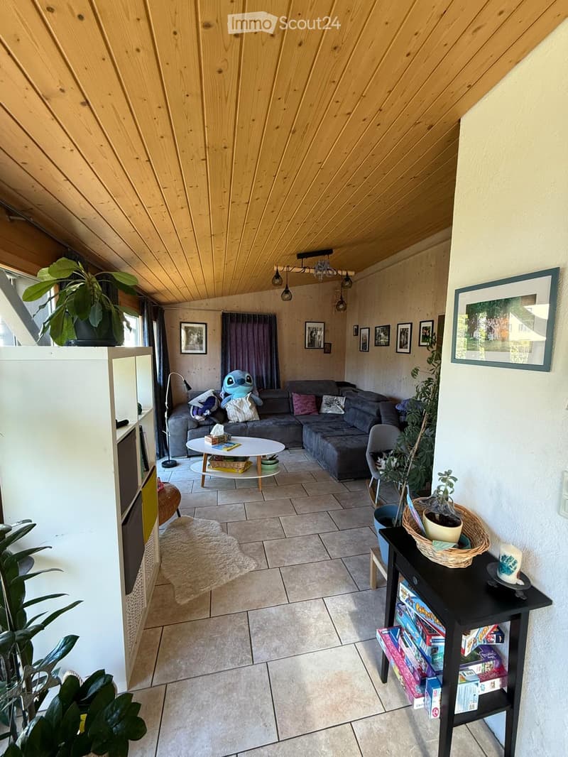 Living room with a grey sectional sofa, coffee table, small round table, and various decorative items including plants and picture frames.