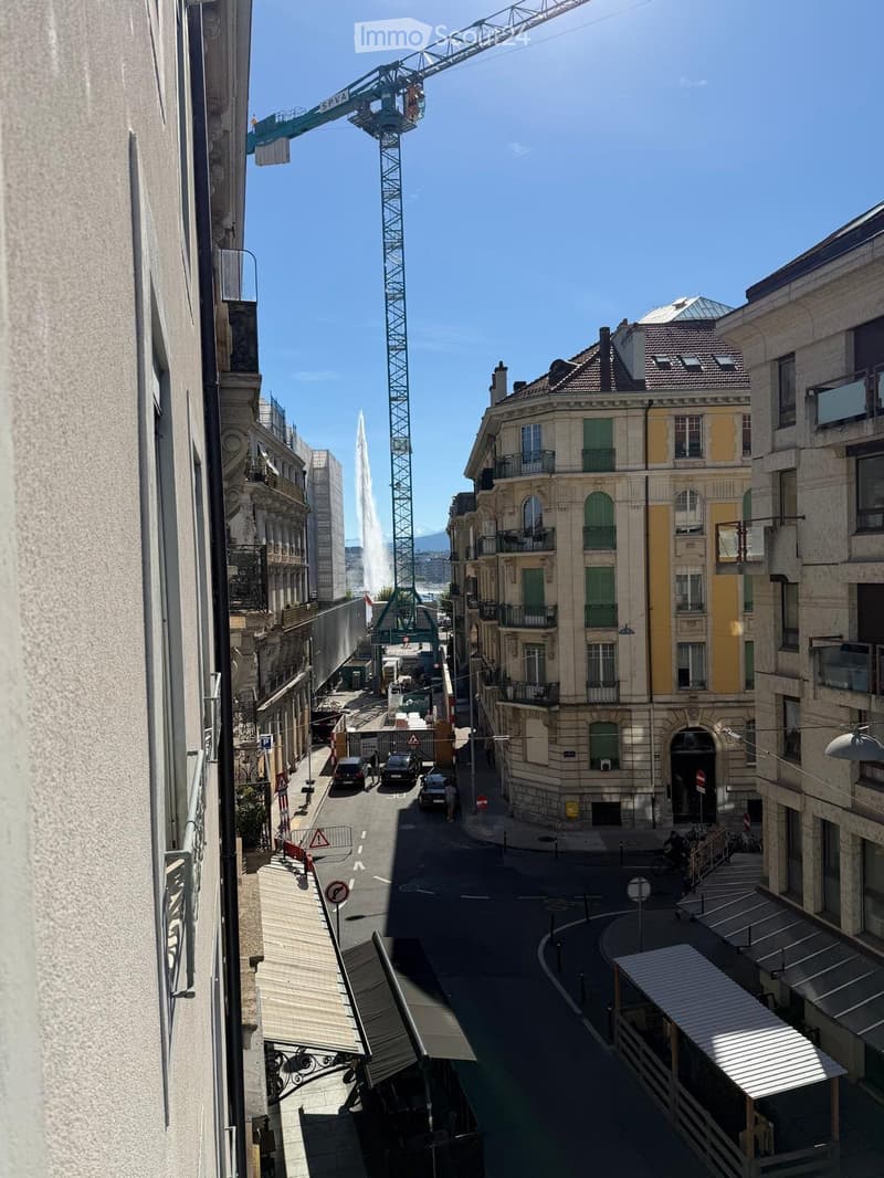 View from a balcony showing a city street with classic European architecture, a fountain, and a construction crane in the background.