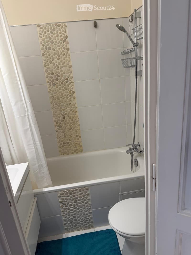 Modern bathroom with a bathtub, toilet, and a shower area featuring a stone accent wall and a white shower curtain.