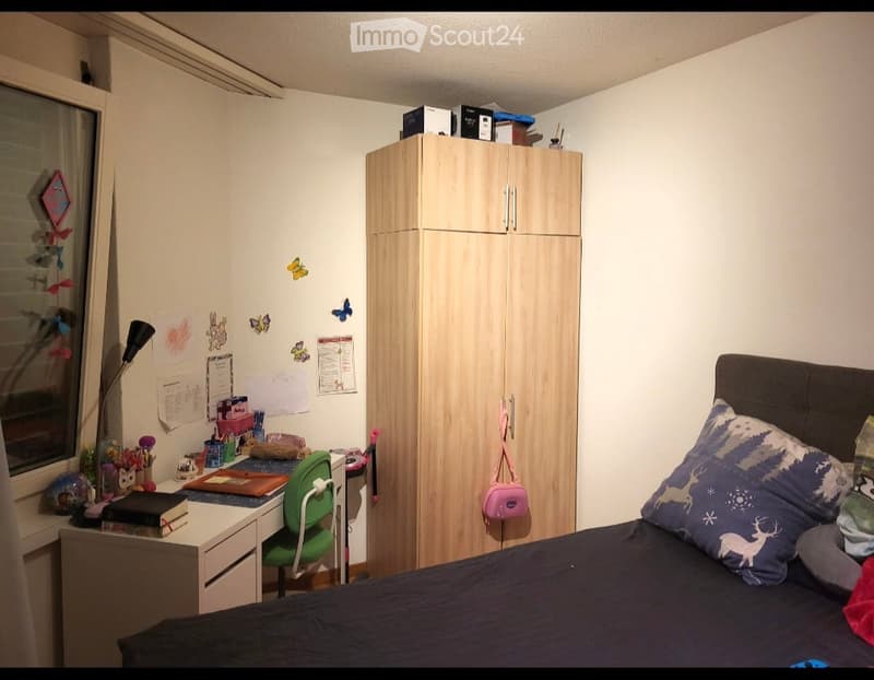 Cozy bedroom with a bed, wardrobe, desk, chair, and various decorative items on the walls and desk.