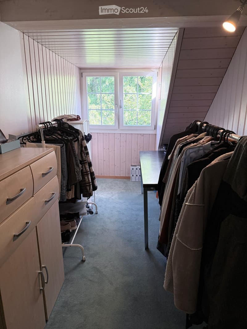 Well-lit hallway with wooden paneling, clothing racks on both sides, a small table in the center, and a drawer unit on the left.