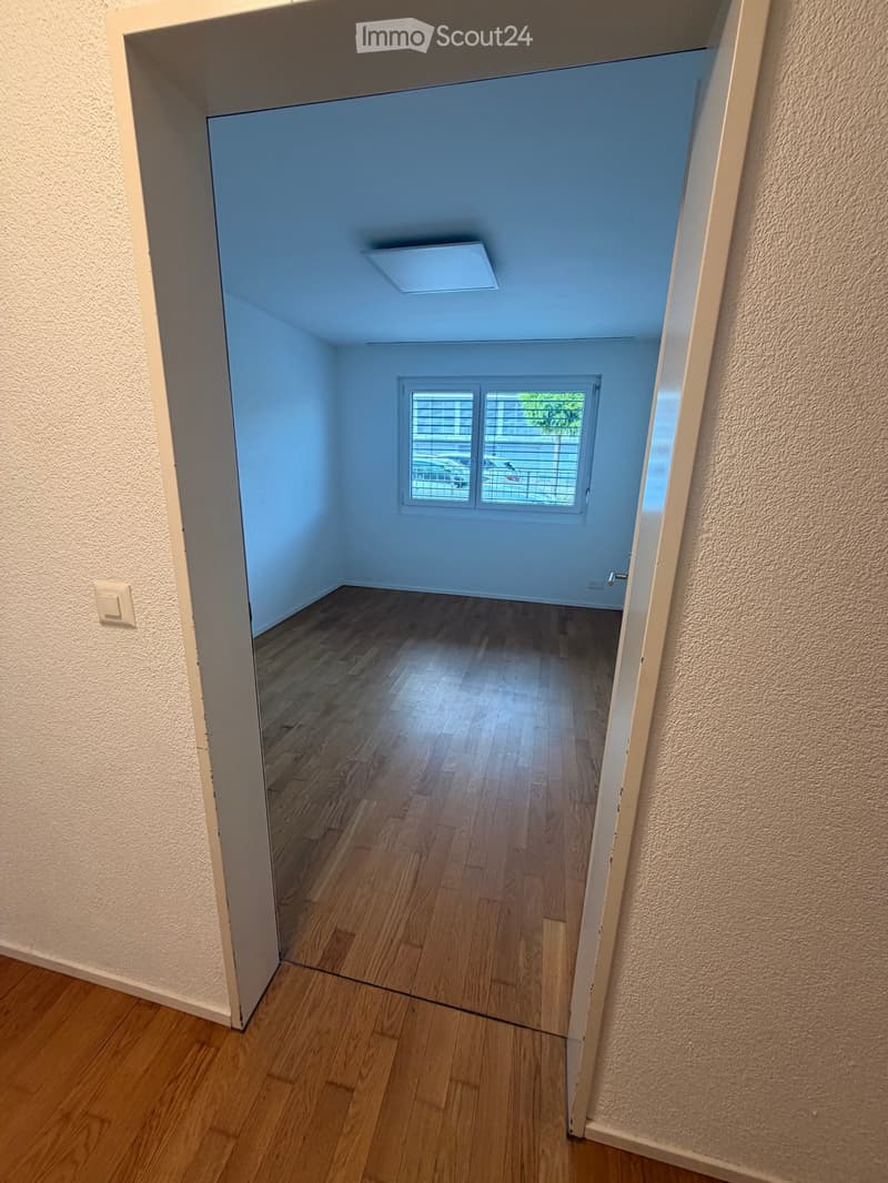 Empty room with wooden flooring, light blue walls, and a window with blinds. No furniture or equipment is present.