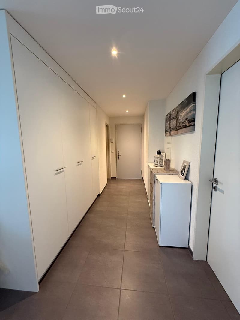 Clean, modern hallway with tiled flooring, white walls, built-in storage units, and a small console table with decorative items.