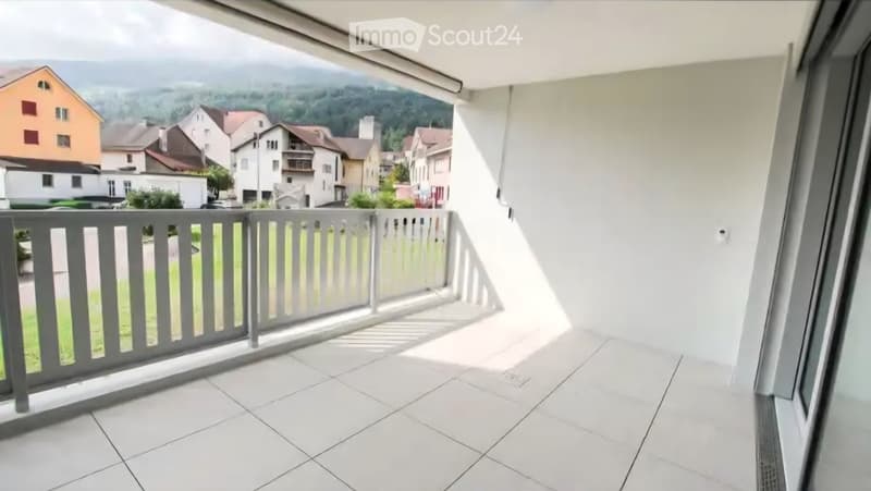 Balcony with white tiled floor, grey railing, and scenic view of a town and mountains.